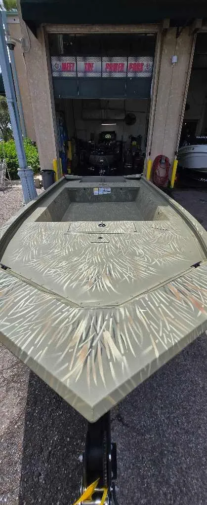 Slide: The Image of 2025 Tracker Grizzly 1754 Jon boat with camouflage pattern, parked outside a garage. - 2