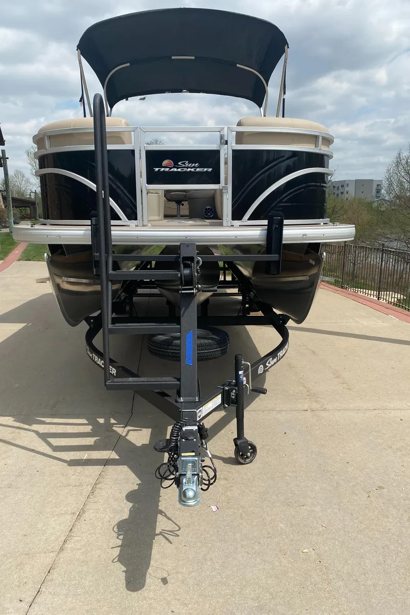 Slide: The Image of 2025 Sun Tracker SportFish 22 XP3 pontoon boat on trailer, parked outdoors. - 2
