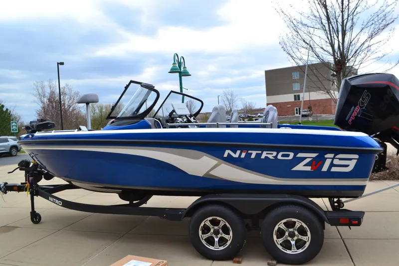 The Image of 2025 Nitro ZV19 Pro boat on trailer, blue and white design, parked outdoors. - 0