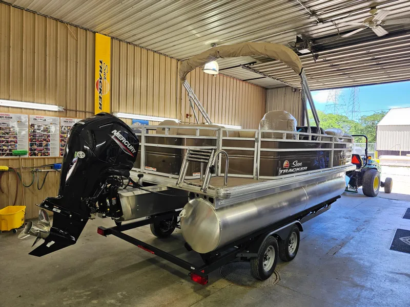 The Image of 2025 Sun Tracker SportFish 20 DLX pontoon boat in a garage, featuring a Mercury outboard motor. - 0