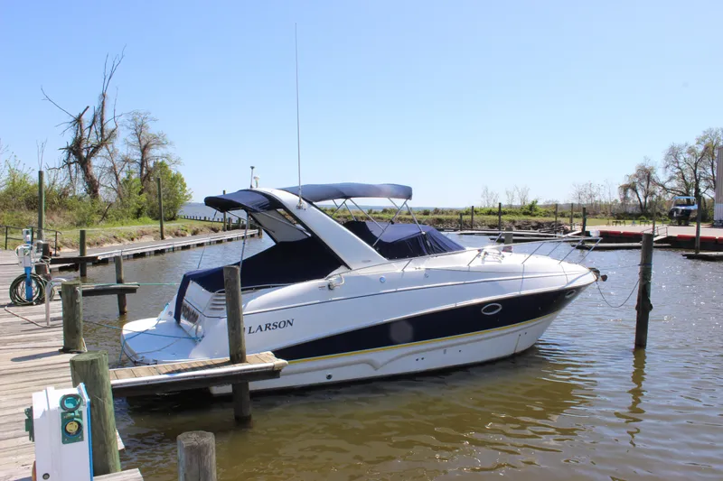 The Image of 2005 Larson Cabrio 310 boat docked at a serene marina under clear blue skies. - 1