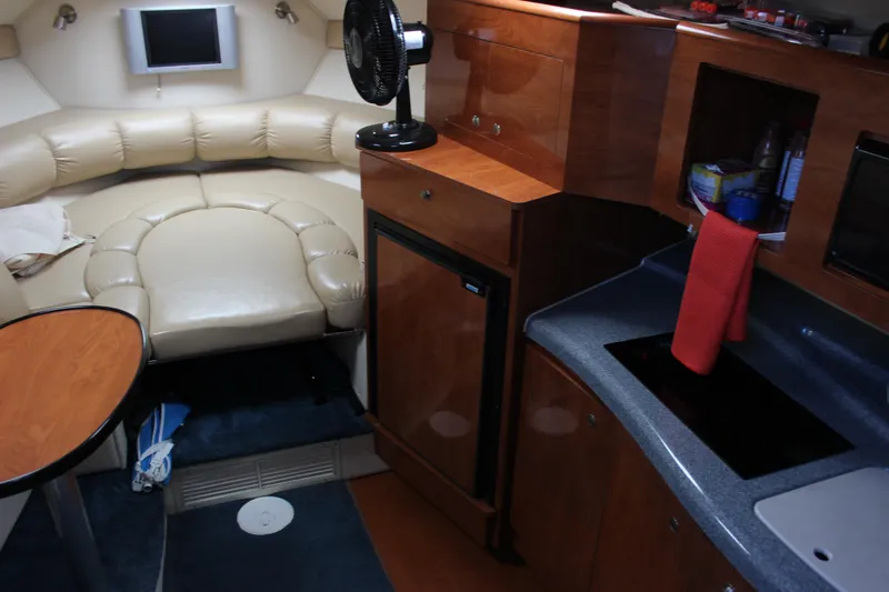 Slide: The Image of 2005 Larson Cabrio 310 cabin interior with kitchenette, seating, and compact fridge. - 18