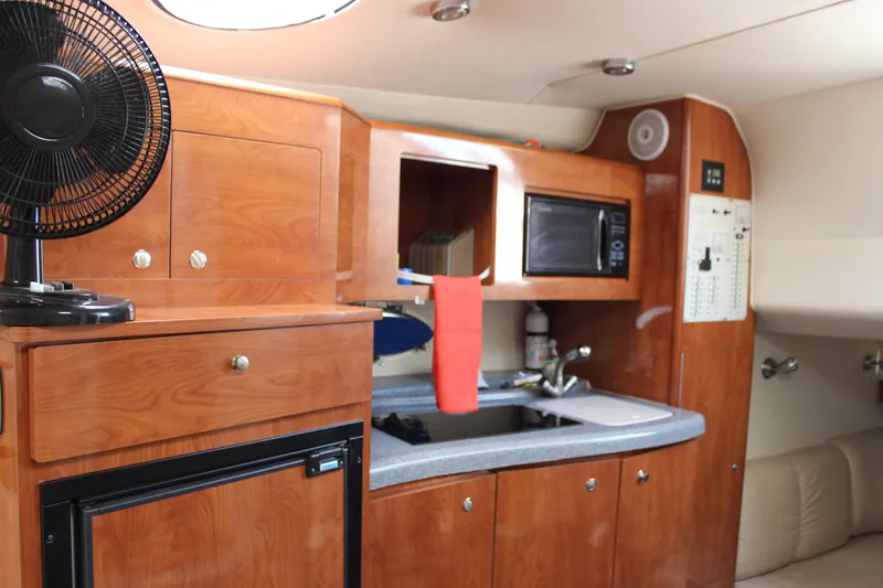 Slide: The Image of 2005 Larson Cabrio 310 cabin interior with wood cabinetry, kitchenette, and appliances. - 23