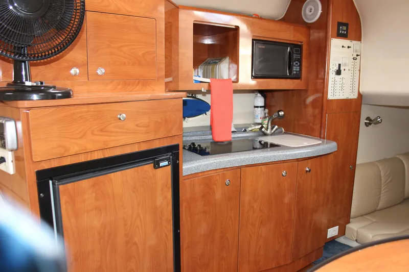 Slide: The Image of 2005 Larson Cabrio 310 boat interior with kitchenette, featuring wood cabinets, microwave, and mini fridge. - 24