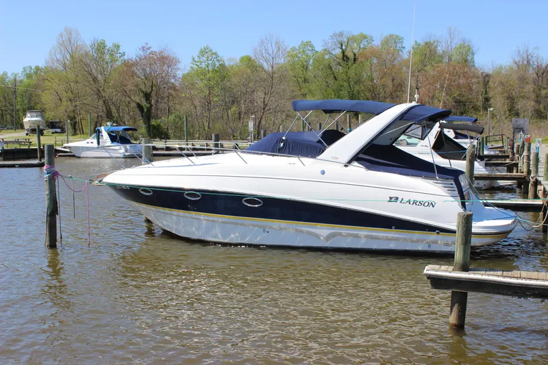 Slide: The Image of 2005 Larson Cabrio 310 boat docked on a calm lake with trees in the background. - 6