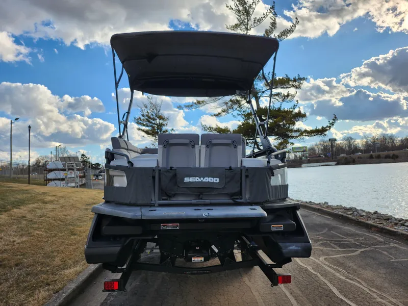 Slide: The Image of 2022 Sea-Doo Switch Sport 21 pontoon boat parked by a scenic lakeside. - 2