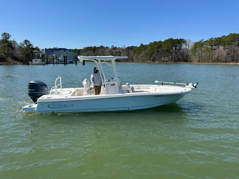 Slide: The Image of 2021 Robalo 246 Cayman boat on calm water, clear sky, and forested shoreline. - 25