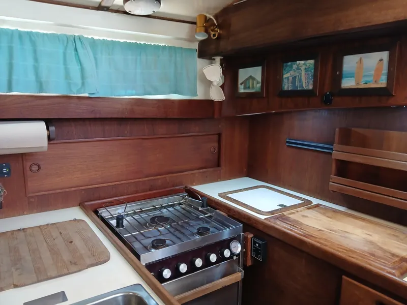 Slide: The Image of 1977 Dickerson 41 yacht kitchen with wooden cabinetry, stove, and turquoise curtains. - 19