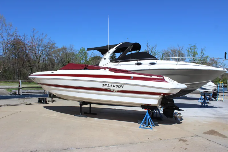 The Image of 2005 Larson LXi 268 boat on stands, red and white design, outdoors on a sunny day. - 0
