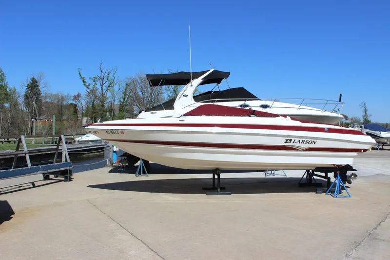 Slide: The Image of 2005 Larson LXi 268 boat on stands, dockside, under clear blue sky. - 1