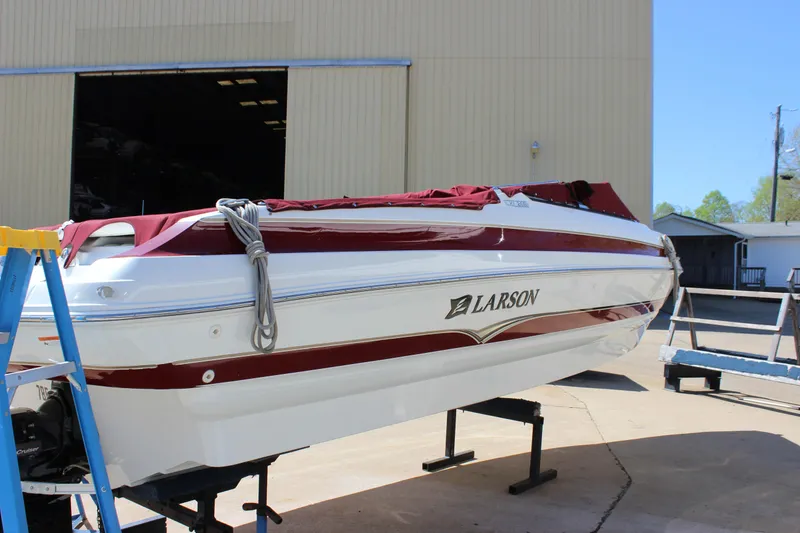 Slide: The Image of 2005 Larson LXi 268 boat with red cover, displayed on a stand outside a warehouse. - 6