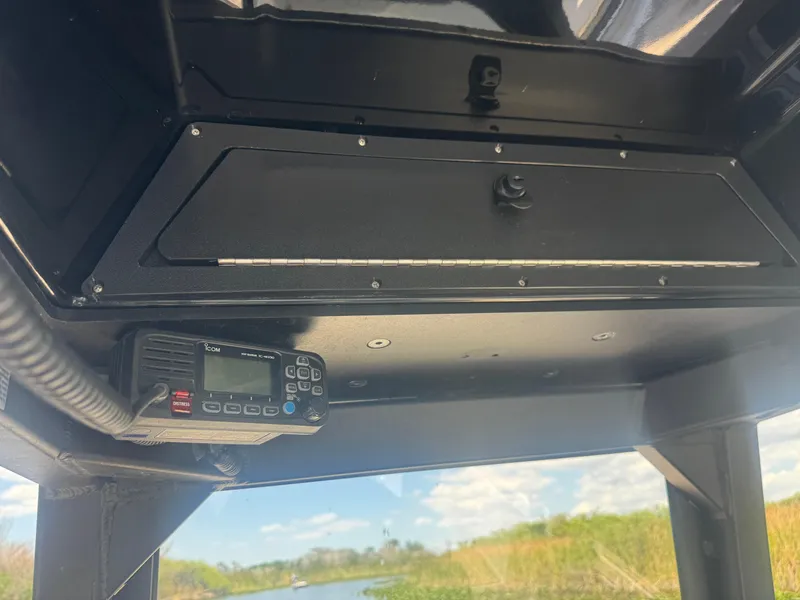 Slide: The Image of 2023 Yamaha Boats 255 FSH Sport E console with radio, storage compartment, and scenic waterway view. - 20