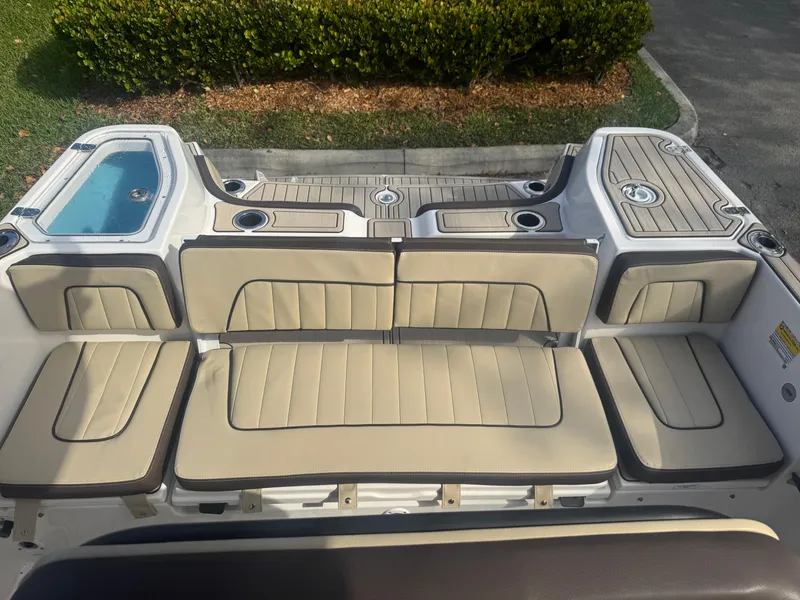 Slide: The Image of 2023 Yamaha Boats 255 FSH Sport E interior seating with beige cushions and storage compartments. - 23