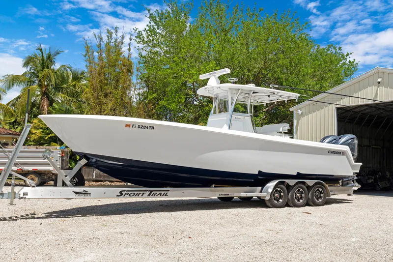 Slide: The Image of 2024 Contender 35 ST boat on trailer, parked outdoors near trees and a building. - 2