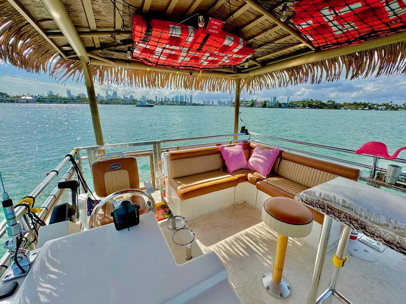 Slide: The Image of Tiki boat interior with seating, tropical decor, and waterfront view; Beachcat COI Tiki Boat 2022. - 12
