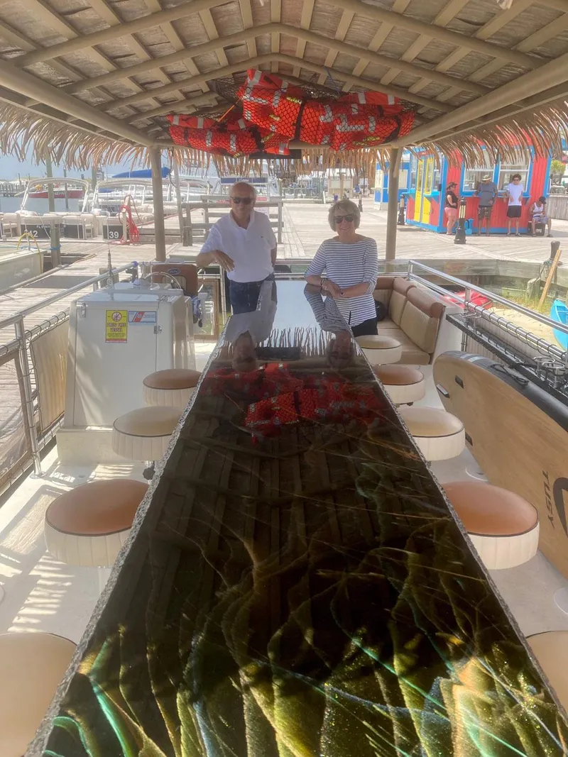 Slide: The Image of 2022 Beachcat COI Tiki Boat with two people onboard, featuring a long table and tropical decor. - 20