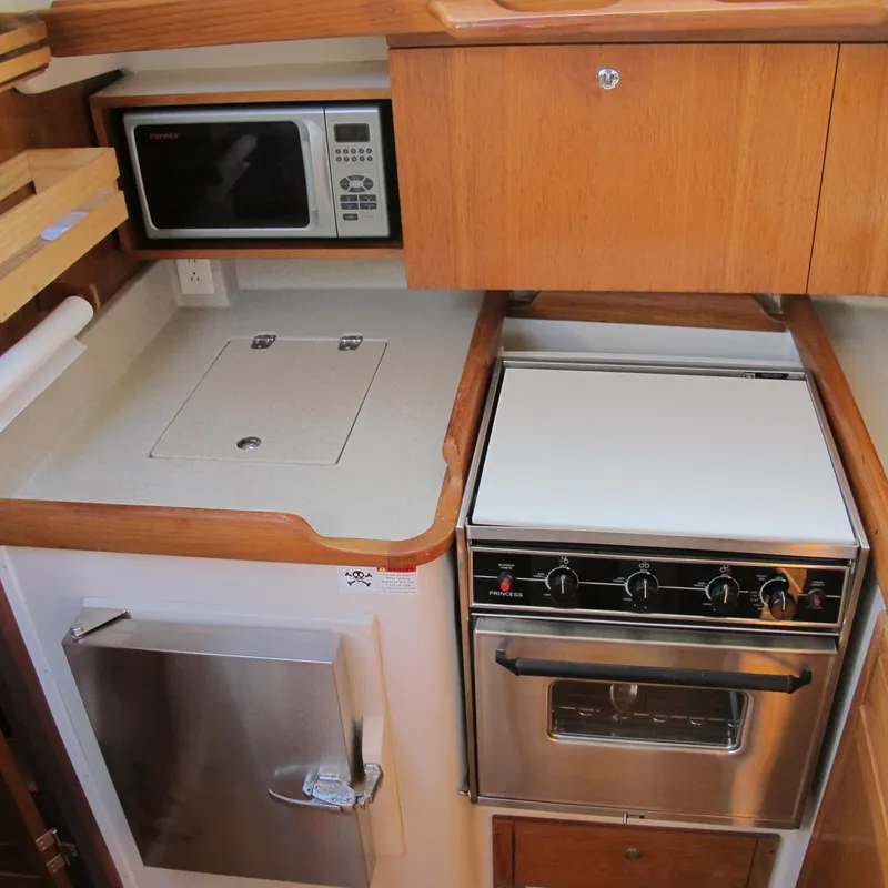Slide: The Image of 2007 Catalina 387 yacht kitchen with stove, microwave, and wooden cabinetry. - 32