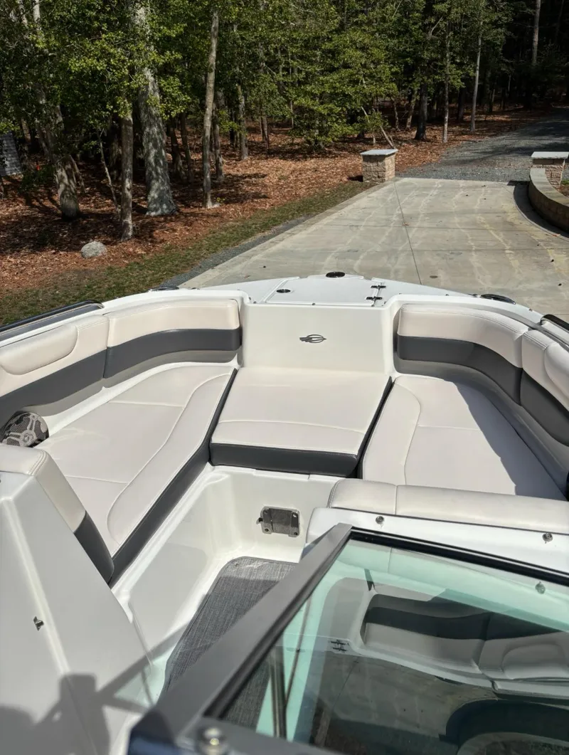 Slide: The Image of 2017 Chaparral 210 Suncoast boat interior with cushioned seating, parked near a wooded area. - 9