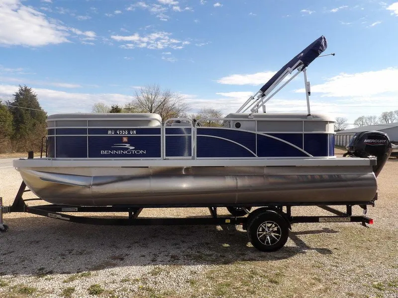 Slide: The Image of 2023 Bennington 20 SVSR pontoon boat on trailer, blue and silver design, parked outdoors. - 4
