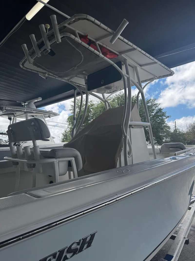 Slide: The Image of 2015 Sailfish 220 CC boat with T-top and rod holders, parked under a canopy. - 4