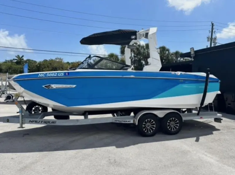 Slide: The Image of 2022 Nautique Super Air Nautique G23 boat on trailer, blue and white design, parked outdoors. - 0