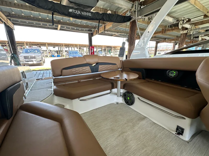 Slide: The Image of 2023 Four Winns HD8 boat interior with brown seating and table under a covered dock. - 20