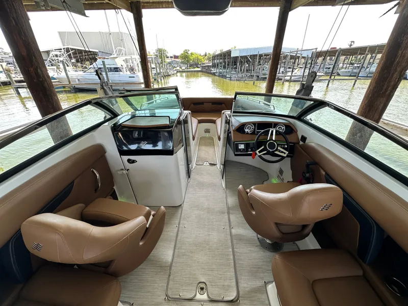Slide: The Image of 2023 Four Winns HD8 boat interior with tan seats and modern dashboard, docked at a marina. - 23