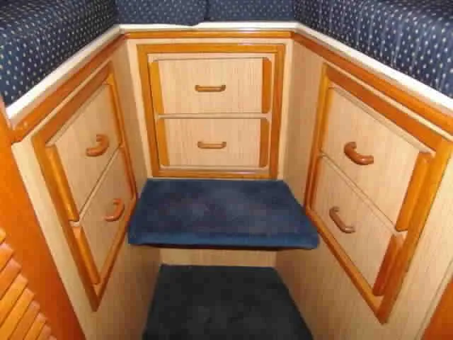 Slide: The Image of 1983 Bertram Sportfisher cabin interior with wooden drawers and blue cushioned seating. - 10