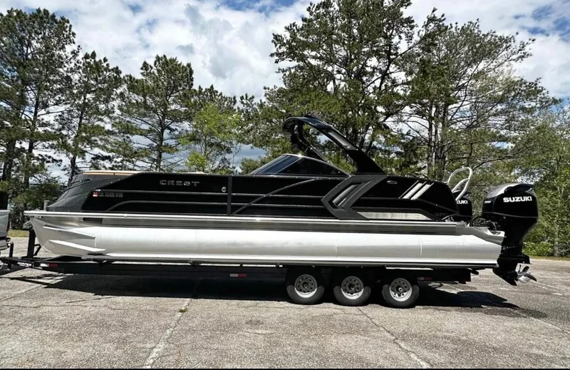Slide: The Image of 2023 Crest Continental NX 270 pontoon boat on trailer, parked outdoors with trees in background. - 1