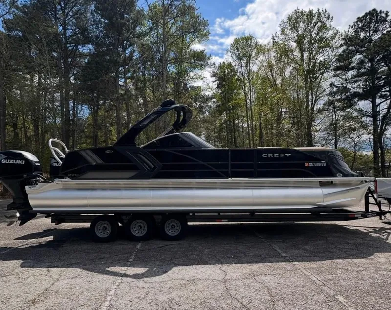 Slide: The Image of 2023 Crest Continental NX 270 pontoon boat on trailer, parked in wooded area. - 19
