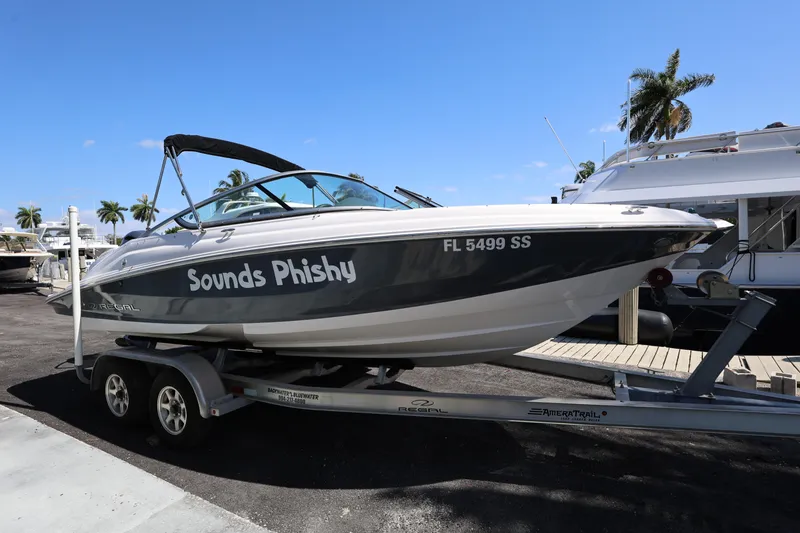 Slide: The Image of 2022 Regal 21 OBX boat named "Sounds Phishy" on a trailer, dockside. - 13