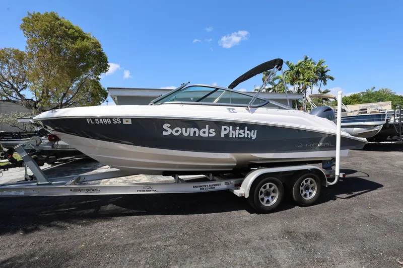 Slide: The Image of 2022 Regal 21 OBX boat named "Sounds Phishy" on a trailer, parked outdoors. - 20
