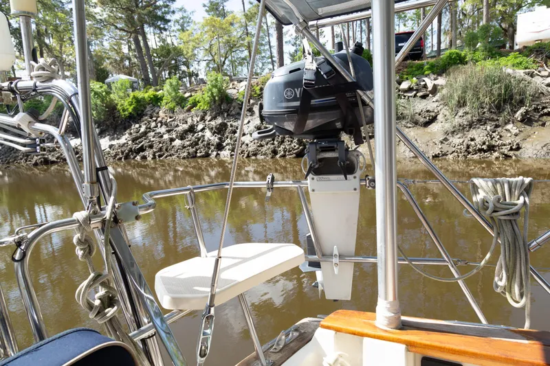 Slide: The Image of Sailboat Island Packet 380, 1999 model, with outboard motor, docked by a wooded shoreline. - 32