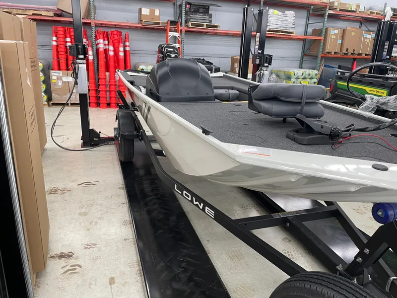 Slide: The Image of 2025 Lowe Skorpion 16 boat in a warehouse, on a trailer, surrounded by equipment. - 2