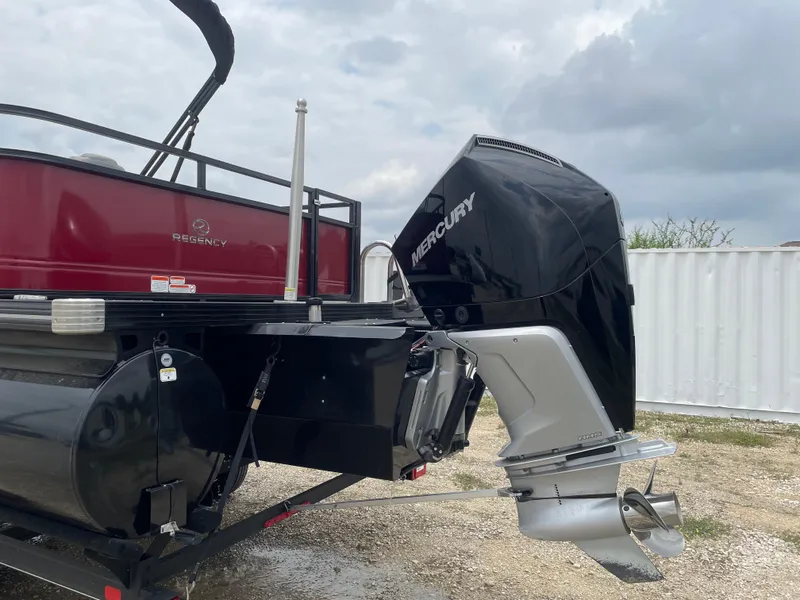 Slide: The Image of 2023 Regency 250DL3 boat with Mercury outboard motor, parked on gravel. - 2
