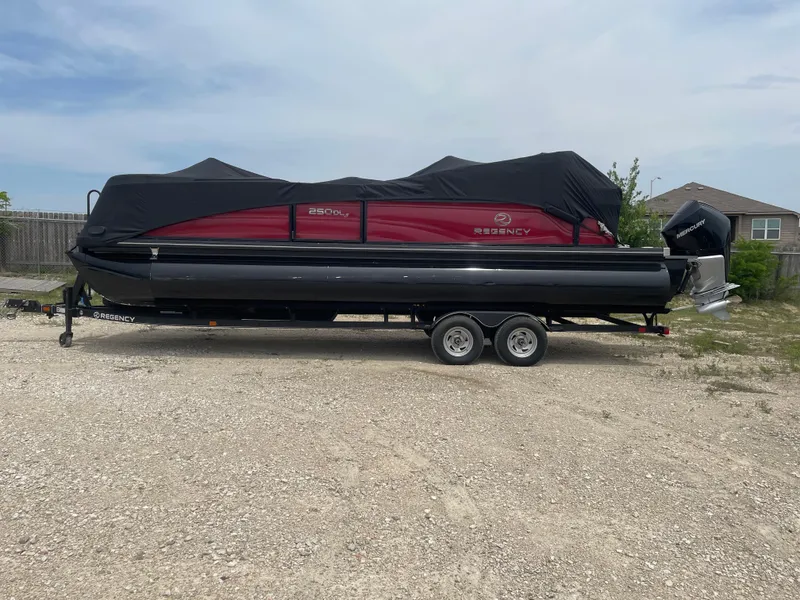 The Image of 2023 Regency 250DL3 pontoon boat on trailer, covered, parked on gravel. - 0