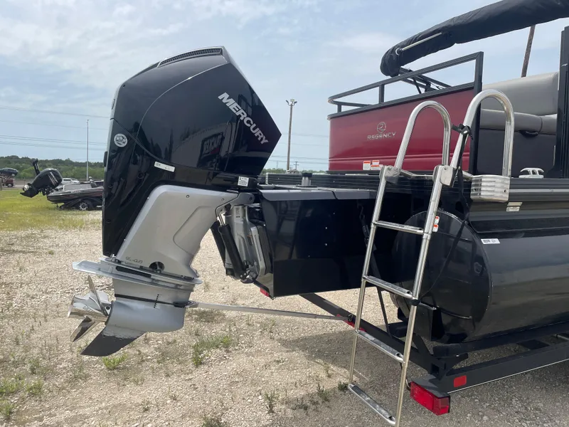 Slide: The Image of 2023 Regency 250DL3 pontoon boat with Mercury outboard motor and ladder, parked on gravel. - 5