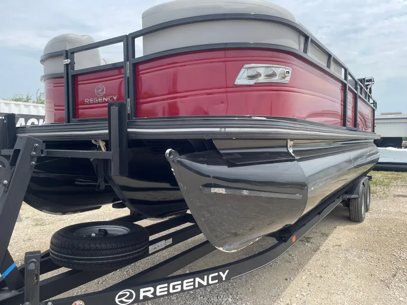 Slide: The Image of 2023 Regency 250DL3 pontoon boat on trailer, red exterior, parked on gravel. - 9