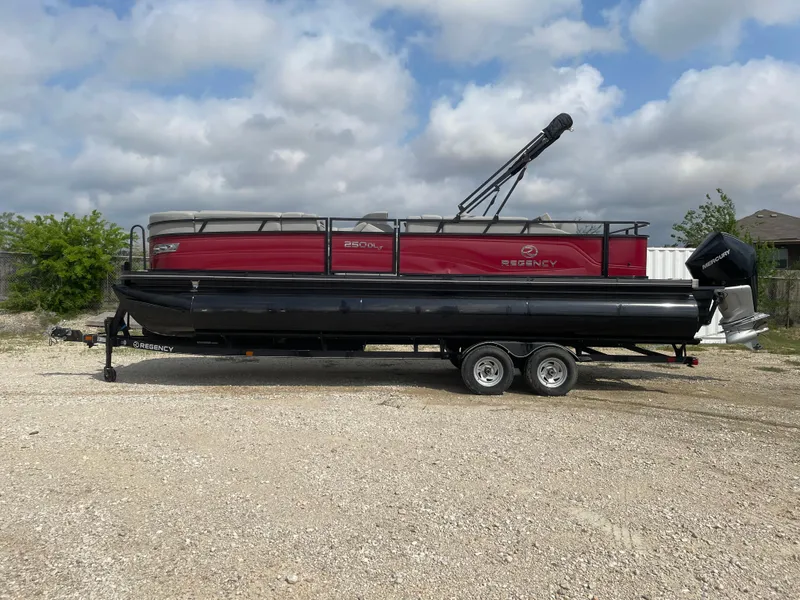 The Image of 2023 Regency 250DL3 pontoon boat on trailer, red and black design, parked outdoors. - 0