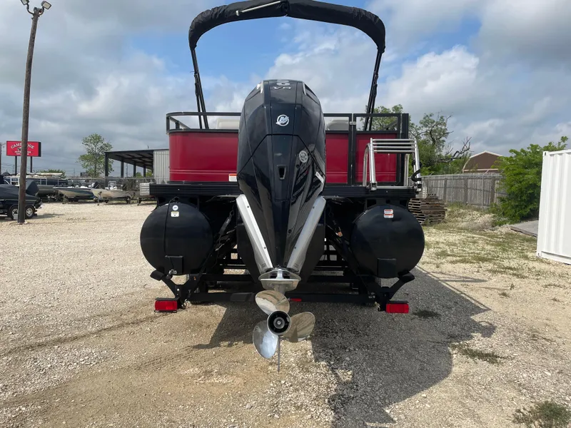 Slide: The Image of 2023 Regency 250DL3 pontoon boat with powerful outboard motor, parked on gravel lot. - 2