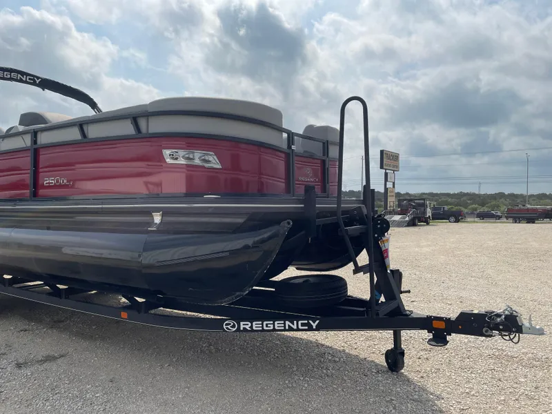 Slide: The Image of 2023 Regency 250DL3 pontoon boat on trailer, parked outdoors under cloudy sky. - 5