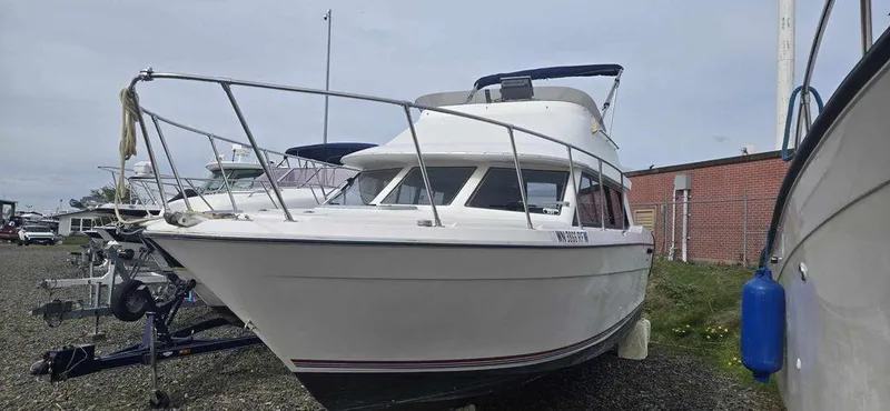 Slide: The Image of 1994 Bayliner 2858 Cierra boat on land, white exterior, parked near a brick building. - 2