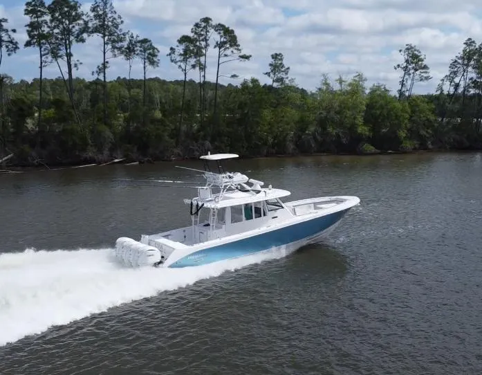 Slide: The Image of 2016 Everglades 435 Center Console boat cruising on a river with lush forest backdrop. - 2