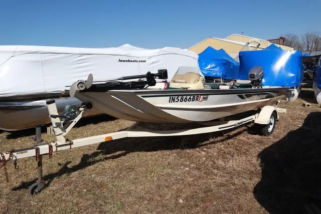 Slide: The Image of 1999 Lowe 170 boat on trailer, parked outdoors, with protective covers in background. - 1