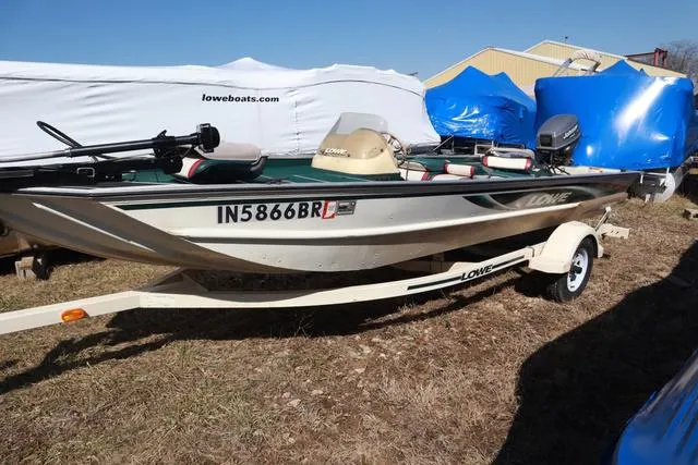 Slide: The Image of 1999 Lowe 170 boat on trailer, parked outdoors, with protective covers in background. - 9