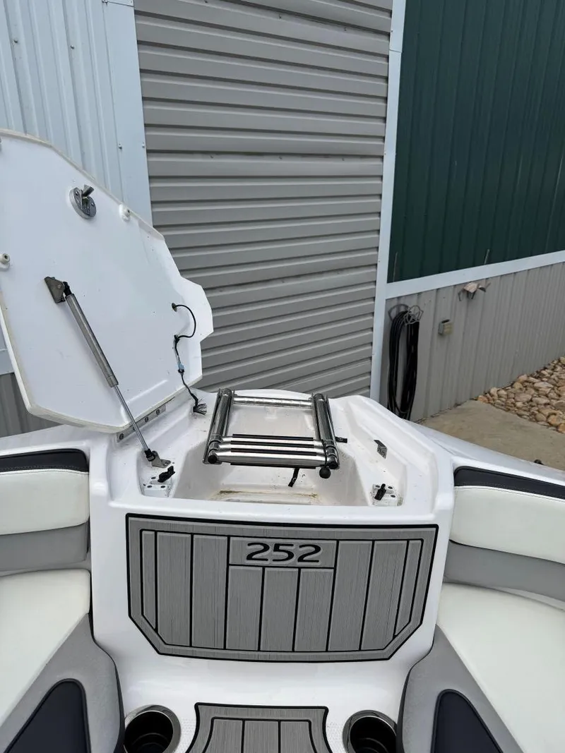 Slide: The Image of 2021 Yamaha Boats 252SE with open storage compartment, docked near a metal building. - 42