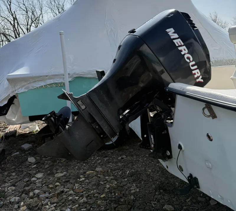 Slide: The Image of 2010 May-Craft 1800 Skiff with Mercury outboard motor, parked on rocky ground. - 5
