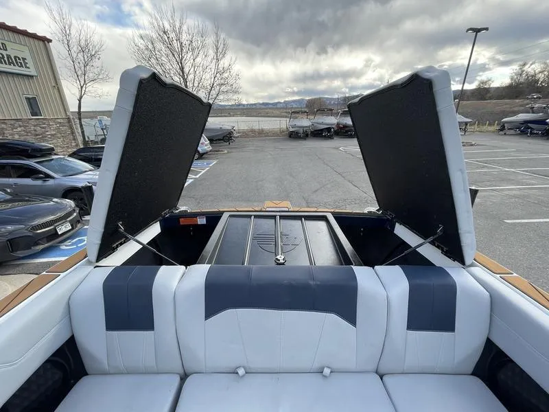 Slide: The Image of 2025 Malibu 20 VTX boat with open storage compartments, parked near a lake. - 20