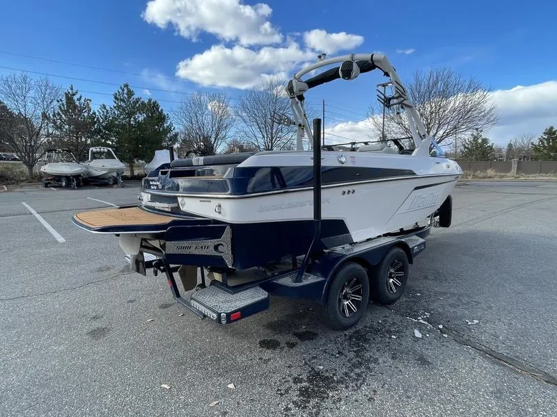 Slide: The Image of 2025 Malibu 20 VTX boat on trailer in parking lot under blue sky. - 6