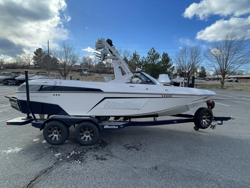 Slide: The Image of 2025 Malibu 20 VTX boat on trailer in parking lot, under cloudy sky. - 7
